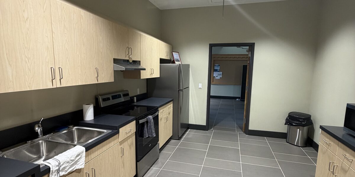 The terminal kitchen, with light wood cabinets, a double sink, a range, a microwave and a full-size refrigerator